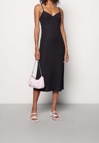 Abito midi nero con spalline sottili e davanti plissettato, abbinato a una borsa rosa con motivo e sandali bianchi con tacco quadrato e cinturini.