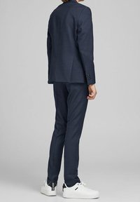 Completo blu navy con giacca sagomata e pantaloni affusolati, realizzato in tessuto liscio. Abbinato a sneakers bianche con dettagli neri.