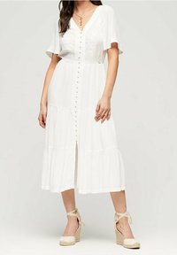 Biała midi sukienka z krótkimi bufkami, z przodu na guziki, w warstwowy wzór i lekką teksturę. W połączeniu z beżowymi espadrylami na obcasie.
