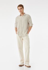 Leichte, gestreifte Hemdbluse in Creme und Marineblau. Kombiniert mit Cremepants und Sneakers mit braunen Sohlen. Glatte Textur.