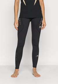 Czarne legginsy o dopasowanym kroju, z kontrastowymi bocznymi akcentami, płaskimi szwami i detalami z logo. Gładka, elastyczna tekstura tkaniny.
