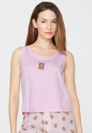 Jeune femme portant un top sans manches lilas avec un petit imprimé ourson et un pantalon de pyjama rose assorti avec des motifs d'oursons.