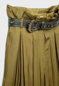 Pantalon plissé taille haute vert olive avec une ceinture en cuir noir ornée d'œillets argentés et d'une boucle argentée.