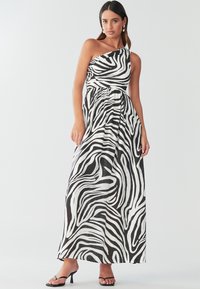 Maxikleid mit Schwarz-Weiß-Zebra-Print, einseitigem Design, geraffter Taille, fließendem Stoff und schwarzen Riemchensandalen.