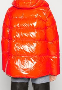 Puchowa kurtka w błyszczącym, jasnopomarańczowym kolorze z poziomymi, pikowanymi sekcjami. Posiada kaptur i elastyczne mankiety, wykonana z gładkiego, refleksyjnego materiału.