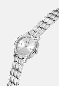 Silberne Uhr mit rundem Zifferblatt, strukturiertem silbernen Ziffernblatt, Kristallakzenten und einem Metallgliedarmband. Markenname "GUESS" auf dem Zifferblatt angezeigt.