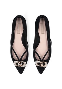 Des ballerines en suède noir avec un bout pointu, dotées d'une boucle décorative en or avec des pierres claires et de lanières croisées sur les côtés.