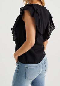 Musta paita, jossa on poimutetut röyhelöhihat, teksturoitu kangas ja tiukka leikkaus. Yhdistettyinä vaaleansinisiin farkkuihin, jotka näyttävät rennolta.