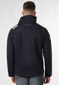 Chaqueta impermeable de color azul marino con alto collar, logo en el hombro, acento verde y tejido texturizado, diseñada para su uso en exteriores.