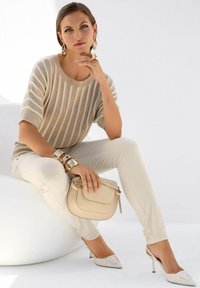 Beige gestreepte top, crème strakke broek en lichtbeige slingback hakken. Accessoires zijn een gestructureerde handtas en gouden armbanden.