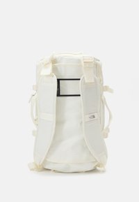 Sac à dos blanc avec des bretelles réglables, poche en mesh à l'avant et zips sur les côtés. Fabriqué en tissu durable avec une texture lisse.