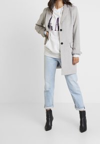 Light gray coat with black buttons, layered over a light gray hoodie and light blue rolled-up jeans. Black ankle boots complete the outfit.