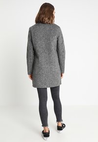 Grå uldfrakke med en lige silhuet, lange ærmer og en ren halsudskæring, parret med mørke smalle jeans og sorte sneakers.