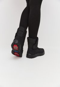 Botas negras de tobillo con un exterior acolchado, con una cremallera en el lado y suela gruesa texturizada con acentos en rojo y azul.