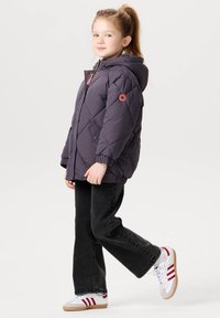 Lilla quilted puffer jakke med hætte, har en pink accentknap, båret over sorte flared jeans og hvide sneakers med røde striber.