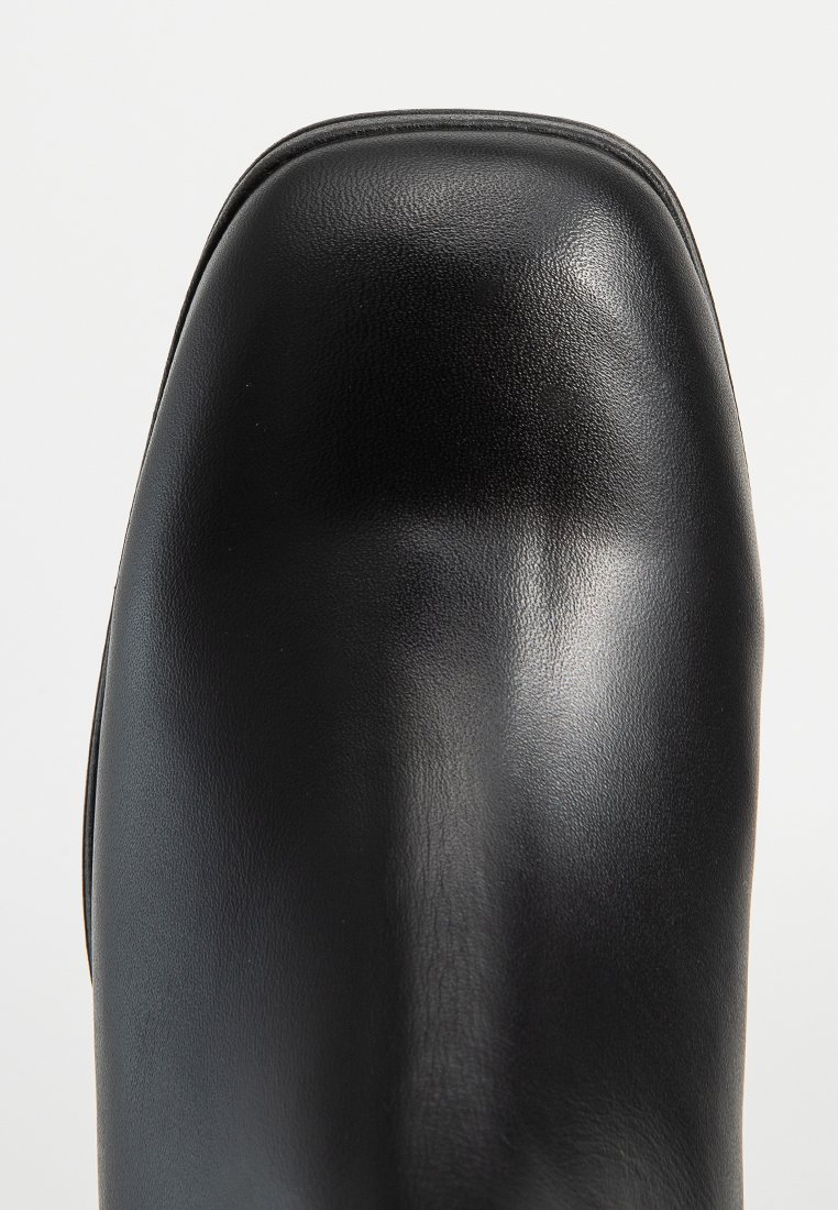 Fekete bőr bokacsizma lekerekített orral és sima textúrával. Minimális varrás részletekkel és letisztult sziluettel rendelkezik.
