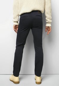 Pantalons slim-fit bleu marine avec une texture lisse et des poches arrière, associés à un pull en tricot de couleur claire et des chaussures beiges.