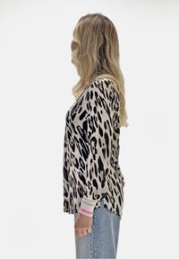 Leopardenmuster-Top mit lockerem Schnitt, schwarz-beiger Farbgebung und gerippten Bündchen mit pinken Akzenten. Kombiniert mit hellblauen Jeans.