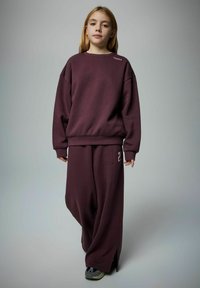 Bordo oversized dukserica i odgovarajuće hlače s razderanim stranama. Dukserica ima bijeli natpis na ramenu; meka tekstura.