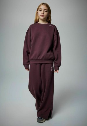 Sweatshirt oversize bourgogne et pantalon assorti avec fentes sur les côtés. Le sweatshirt présente un texte blanc sur l'épaule ; texture douce.