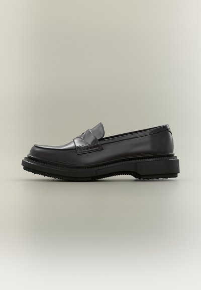 Μαύρο δερμάτινο μοκασίνι με χοντρή σόλα και διακοσμητική ραμμένη λωρίδα στην επάνω πλευρά, εμφανίζεται σε πλευρική προβολή σε ουδέτερο φόντο.