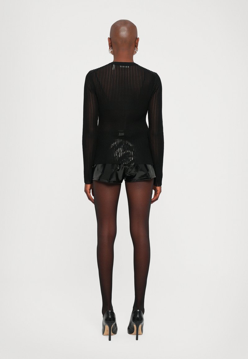 Schwarzes gestreiftes Langarmoberteil mit transparentem Design, kombiniert mit glänzenden schwarzen Rüschenshorts und schwarzen Strumpfhosen, getragen mit High Heels.