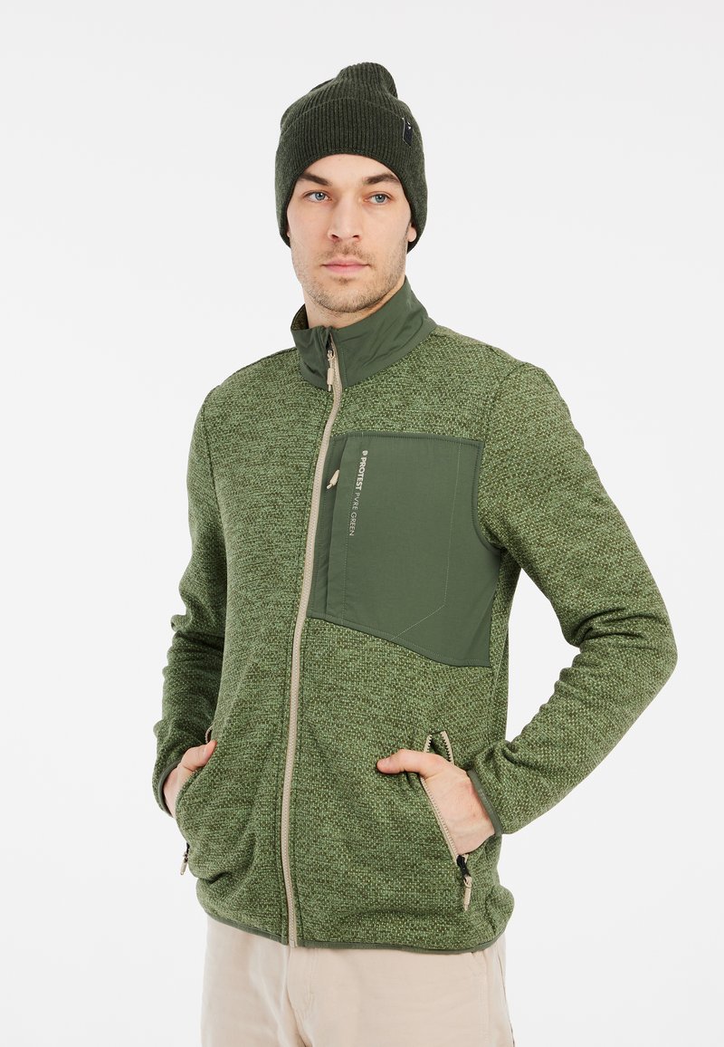 Groene fleecejas met een rits aan de voorkant, hoge kraag, borstzak en twee zijzakken met rits. Gebreide textuur, aangevuld met een bijpassende muts.