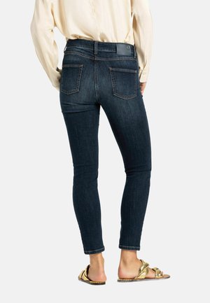Dunkelblaue Skinny-Jeans mit hoher Taille, Fünf-Taschen-Design und glatter Textur, kombiniert mit goldenen flachen Sandalen.