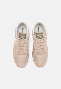 Beige Saucony Jazz joggesko med overdel i suede og tekstil, hvite detaljer, rund tå, snørelukking og polstret krage med logomerker.