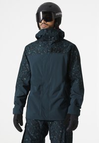 Waterproof ski jacket with a dark teal body, patterned sleeves, high collar, and logo. Matched with black gloves, showcasing a functional design.