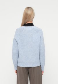 Gaiši zils adīts džemperis ar teksturētu apdari, raglāna piedurknēm un ribotu apakšmalu. Nēsāts virs melna krekla ar apkakli.