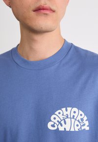 Kék pamut póló kerek nyakú, fehér grafikai szövegezéssel, melyen az "CAPARYK WIP" felirat szerepel. Puha tapintás és laza szabás jellemzi.