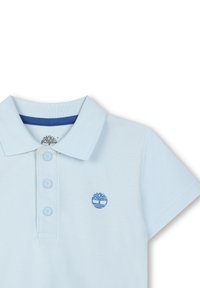 Lichtblauw polo shirt van een gestructureerde stof, met een drie-knopen-overgang en een blauw logo geborduurd op de linkerborst.