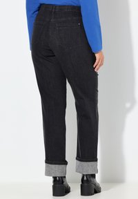 Pantalones vaqueros negros de cintura alta, pierna recta y puños doblados. Cuentan con dos bolsillos traseros y una textura sutil. Combinados con botas negras.