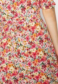 Vestido floral com um padrão diversificado de flores cor-de-rosa, vermelhas e amarelas sobre um fundo claro, com uma cintura atada e mangas bufantes.