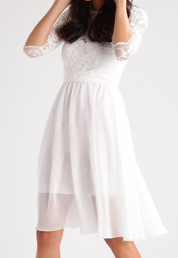 Vit klänning med en spetslivstycke och trekvartsärmar. En flödande chiffongkjol faller nedanför knäet och skapar en lager-effekt.