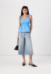 Light blue peplum top with adjustable tie straps, paired with wide-leg light wash denim culottes, black slingback heels, and a small black bag.