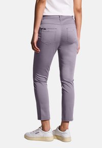 Pantaloni stretch viola con vestibilità slim, cinque tasche e dettagli di cucitura visibili. Indossati con sneakers bianche per un contrasto.