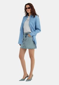 Camicia a righe blu e bianche sopra una t-shirt bianca, abbinata a una minigonna in denim chiaro e scarpe col tacco blue.