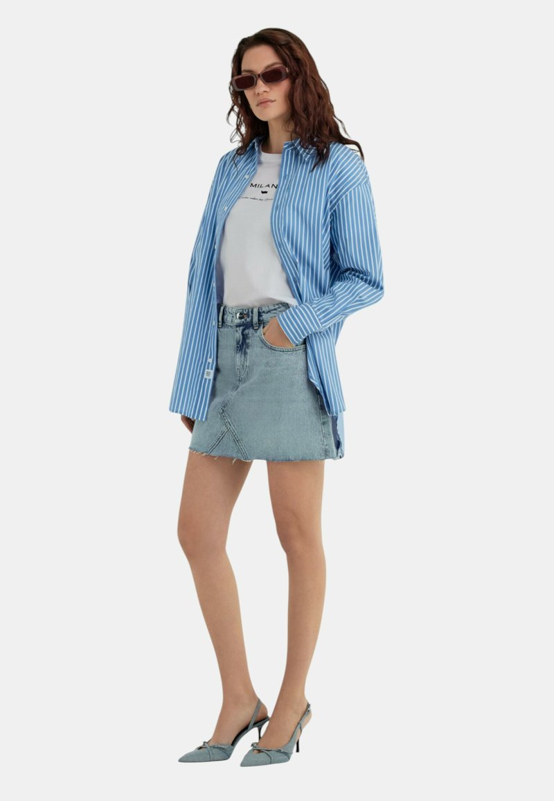 Camicia a righe blu e bianche sopra una t-shirt bianca, abbinata a una minigonna in denim chiaro e scarpe col tacco blue.
