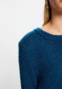 Gebreide trui in levendig blauw met een gestructureerd, verhoogd patroon. Heeft een brede, geribbelde halslijn en een losse pasvorm.
