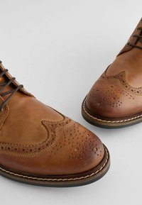 Los zapatos de cuero marrón tipo brogue cuentan con una punta afilada, perforaciones decorativas y costuras en contraste sobre una suela de goma.
