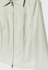 Lysegrå jakke med lynlås foran, spids krave og diskrete syningsdetaljer. Fremstillet af glat, blødt stof.