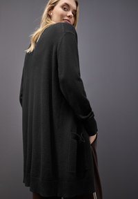 Svart oversized tröja i texturerad tyg med ribbade mudd och fållar, och en synlig sidoficka.