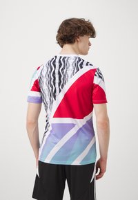 T-shirt de sport à manches courtes présentant des motifs géométriques vibrants en rouge, noir, violet et bleu ; fabriqué en tissu léger et extensible.