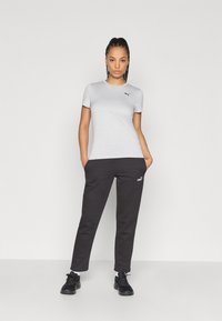 Tricou gri deschis cu mâneci scurte și logo-ul Puma negru, asortat cu pantaloni de trening negri cu logo, și pantofi sport negri.