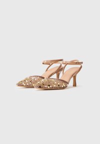 Pár béžových lodičiek na vysokom opätku s členkovými popruhmi, zdobených zlatými korálkami, flitrami a perlami na špicatej časti.