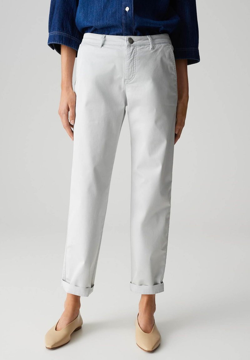 Pantalons en coton gris clair avec des ourlets retroussés, des poches avant et une fermeture à bouton. Assortis à des chaussures beige à enfiler.