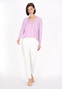 Ljuslila cardigan med V-ringning, knäppning och långa ärmar, kombinerad med vita byxor och beige loafers. Slät textur.