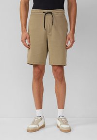 Shorts de sport beiges en tissu texturé avec une taille élastique, fermeture à cordon de serrage et poches latérales. Portés avec des chaussettes blanches et des baskets.